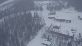 AK0001_1316 - 4K aerial stock footage flying over forest and small warehouse buildings to reveal Eagle River Road overpass, falling snow, Alaska
