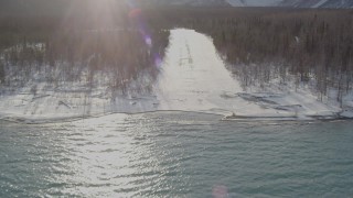 AK0001_1361 - 4K aerial stock footage flying over Eklutna Lake, descending toward snowy strip in woods, Alaska