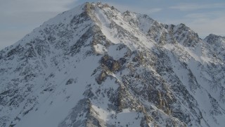 AK0001_1374 - Aerial stock footage of Approach and fly over a rocky, snow covered mountain peak, Chugach Mountains, Alaska