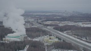 AK0001_1513 - 4K aerial stock footage flying by power plant toward Glenn Highway and shopping center in snow, Anchorage, Alaska
