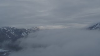 AK0001_1553 - 4K aerial stock footage flying between clouds over Eklutna Lake Valley, Alaska in snow