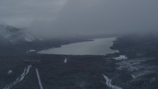 AK0001_1554 - 4K aerial stock footage descending through clouds revealing Eklutna Lake, Alaska in snow