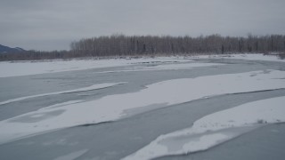 AK0001_1601 - 4K aerial stock footage following an icy river toward snow covered shore, Knik River Valley, Alaska
