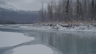 AK0001_1602 - 4K aerial stock footage following an icy river between snowy shore, Knik River Valley, Alaska