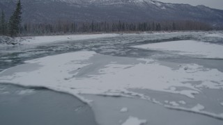 AK0001_1605 - 4K aerial stock footage flying low over icy river toward snow covered shore, Knik River Valley, Alaska
