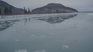 AK0001_1611 - 4K aerial stock footage icy river, snowy shore, reveal Glenn Highway bridge, Knik River Valley, Alaska