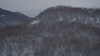 AK0001_1612 - 4K aerial stock footage flying over snow covered, wooded hill revealing Glenn Highway, Anchorage, Alaska