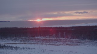 AK0001_1676 - 4K aerial stock footage the sunset behind clouds seen from snow covered Point MacKenzie, Alaska