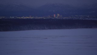 AK0001_1714 - 4K aerial stock footage tilt up from snowy ground revealing Downtown Anchorage skyline, Alaska, night