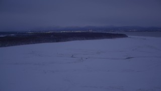 AK0001_1715 - 4K aerial stock footage flying over snow covered ground toward forest at night, Point MacKenzie, Alaska