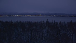 AK0001_1718 - 4K aerial stock footage ascend from snowy trees, reveal Downtown Anchorage, Alaska, night