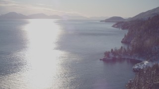 AK0001_1838 - 4K aerial stock footage he sun reflecting off of water in Port Wells next to snowy, wooded shore, Alaska