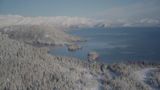 AK0001_1878 - 4K aerial stock footage flying over snowy, wooded shore away from Hummer Bay, Port Wells, Alaska