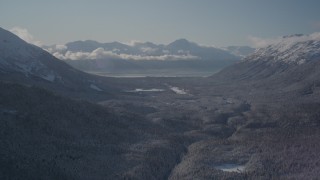 AK0001_1956 - 4K aerial stock footage flying over a wooded valley between snowy Chugach Mountains, Girdwood, Alaska