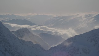 AK0001_1977 - 4K aerial stock footage snowy, windblown mountain ranges and low clouds in Kenai Mountains, Alaska