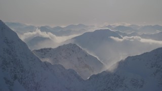 AK0001_1978 - 4K aerial stock footage snowy, windblown mountain ranges and low clouds in Kenai Mountains, Alaska
