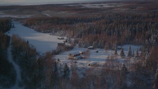 AK0001_2037 - 4K aerial stock footage flying away from cabins in snowy woods in Point MacKenzie, Alaska