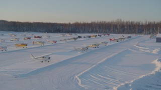 AK0001_2074 - 4K aerial stock footage flying by parked aircraft at snow covered Shawn Field at sunset, Wasilla, Alaska