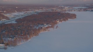 AK0001_2083 - 4K aerial stock footage fly over Lucile Lake, homes on the snowy shore, Wasilla, Alaska, sunset