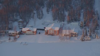 AK0001_2086 - 4K aerial stock footage flying away from snow covered houses on Lucile Lake at sunset, Wasilla, Alaska