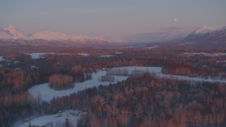 AK0001_2095 - 4K aerial stock footage fly over snowy rural homes, reveal moon over mountains, Palmer, Alaska, twilight