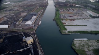 AX0001_170 - Aerial stock footage of 4.8K aerial  video tilt from bird's eye of petroleum coke by the Calumet River, revealing more industrial buildings, East Side Chicago, Illinois