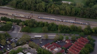 AX0003_022 - 4.8K aerial stock footage of tracking a commuter train traveling through Kenwood at twilight, reveal apartments and strip mall, Chicago, Illinois