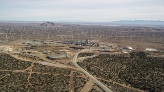 AX0006_029E - 5K stock footage aerial video approach and orbit quarry surrounded by wind farm windmills in the Mojave Desert, California