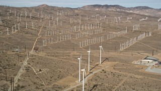 AX0006_042 - 5K aerial stock footage of a wide orbit around rows of windmills at a desert wind energy farm in California