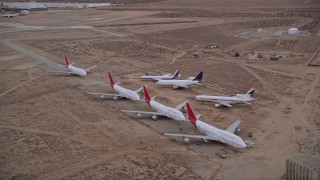 AX0007_013 - 5K stock footage aerial video orbit seven airliners parked at aircraft boneyard in Sunset, Victorville Airport, California