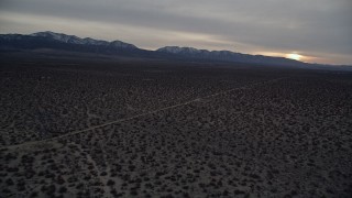 AX0007_033E - 5K aerial stock footage fly over Mojave Desert and approach mountains with snow at twilight, California