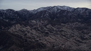 AX0008_004 - 5K aerial stock footage tilt from dry riverbed to reveal rock formations and snowy San Gabriel Mountains at twilight, California