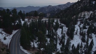 AX0008_018E - 5K aerial stock footage fly over lonely mountain road with winter snow through San Gabriel Mountains at twilight, California