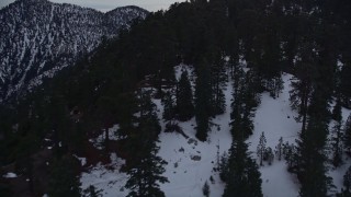 AX0008_030E - 5K aerial stock footage fly over the San Gabriel Mountains with winter snow and trees at twilight, California