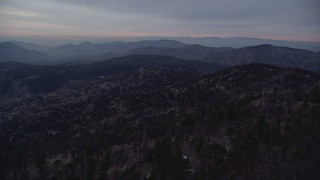 AX0008_034 - 5K aerial stock footage fly over mountain with trees and snow patches, San Gabriel Mountains at twilight, California
