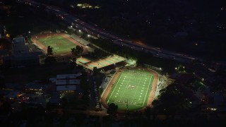 AX0008_067E - 5K stock footage aerial video approach and orbit football and track fields at night in La Cañada Flintridge, California