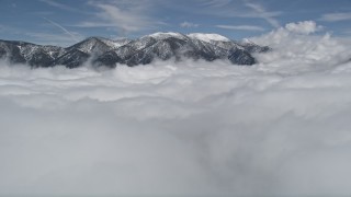 AX0009_108E - 5K aerial stock footage tilt up from clouds to reveal snowy San Bernardino Mountains, California