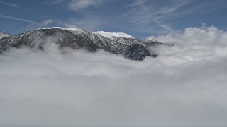 AX0009_110E - 5K aerial stock footage approach snowy San Bernardino Mountains and fly over clouds in winter, California