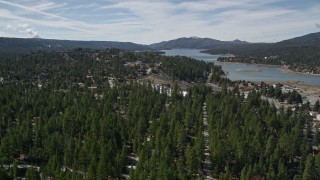 AX0010_004E - 5K aerial stock footage fly over homes hidden by trees and tilt to reveal Big Bear Lake, California