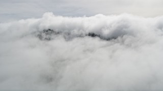 AX0010_091E - 5K aerial stock footage approach peak with light snow covered by clouds in the San Jacinto Mountains, California