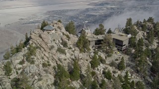 AX0010_106E - 5K aerial stock footage orbit a rocky summit to reveal the Palm Springs Tramway in the San Jacinto Mountains, California