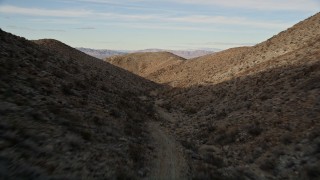AX0011_055E - 5K aerial stock footage of flying over a dirt road through a desert canyon, Mojave Desert, California