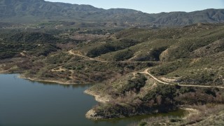 AX0014_032 - 5K aerial stock footage fly over lake shore toward a country road in the hills, Lake Hemet, California