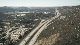 AX0015_006E - 5K aerial stock footage follow light traffic on an interstate through hills near greenhouses, Temecula, California
