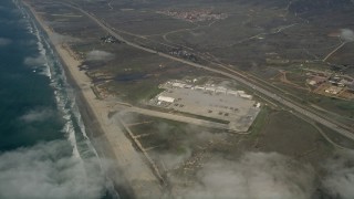 AX0016_023 - 5K aerial stock footage approach and tilt to Camp Pendleton by the coast, seen through the clouds, California