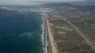 AX0016_026 - 5K aerial stock footage of following an empty beach to approach small military airfield, Mcolf Camp Pendleton, California