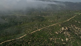 AX0016_063 - 5K aerial stock footage fly over and pan across a dirt road on a hill near rolling fog, Laguna Beach, California