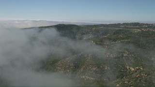 AX0016_067 - 5K aerial stock footage fly over fog over green hills near hilltop homes in Newport Beach, California
