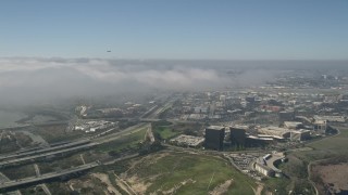AX0016_079 - 5K aerial stock footage track an airliner ascending over a fog bank, seen from office buildings beside Highway 73, Newport Beach, California