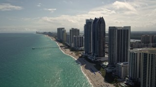AX0020_084E - 5K aerial stock footage of passing beachfront high-rises to approach a pier in Sunny Isles Beach, Florida